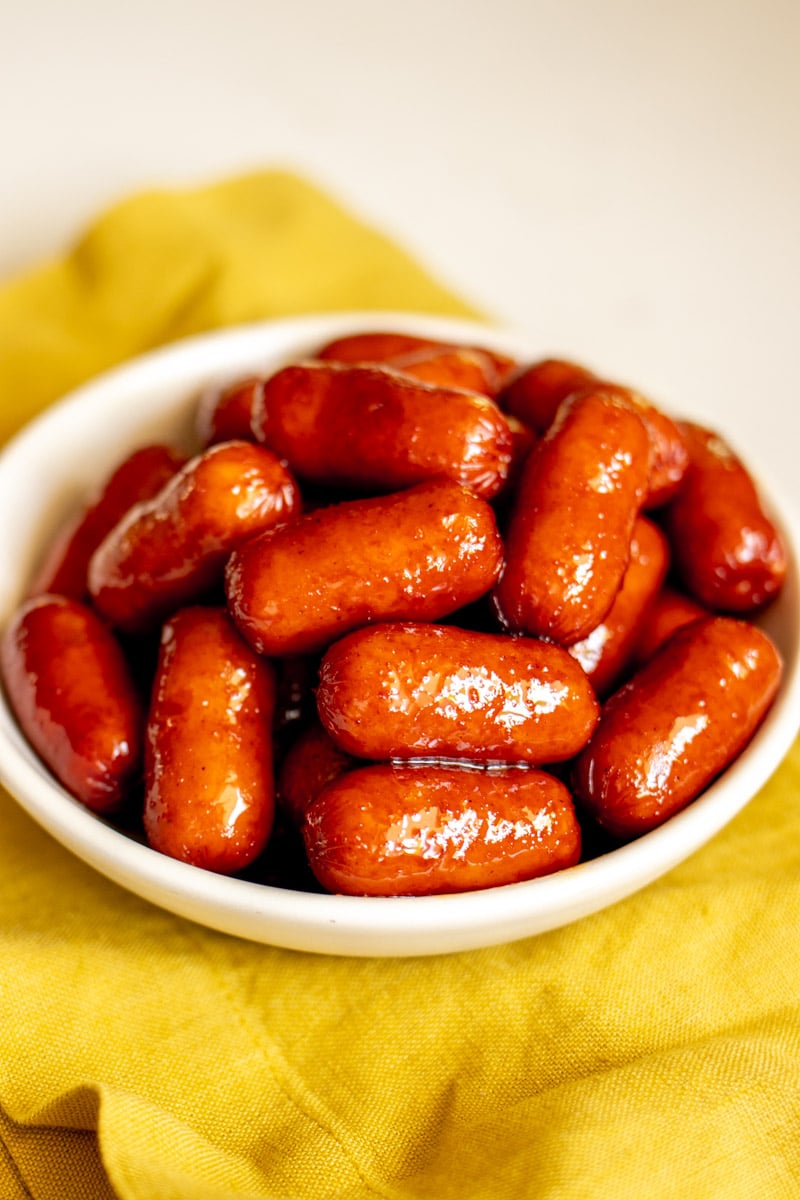 a birds eye view of cocktail sausages in a white bowl with a yellow napkin underneath.