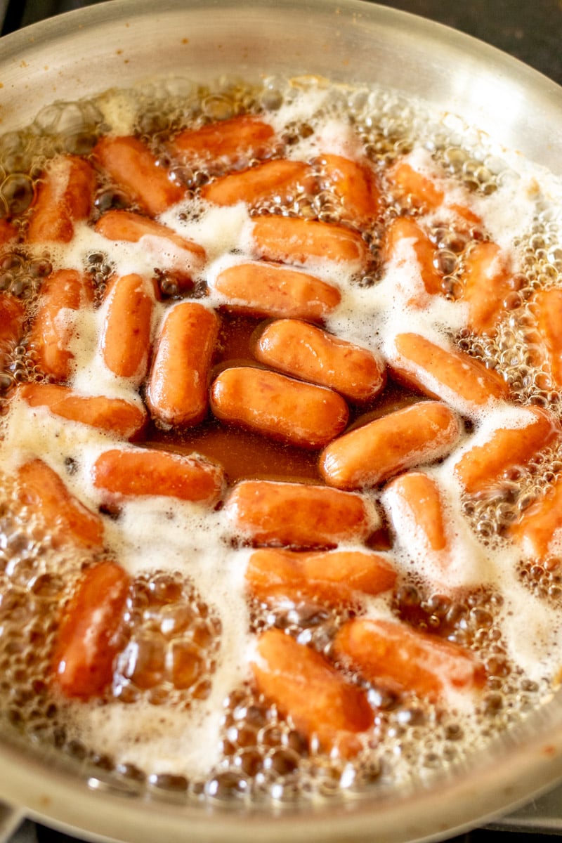 an overhead view of a frying pan full of beer and cocktail sausages.