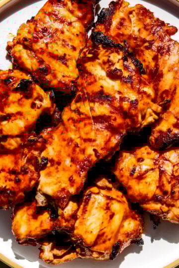 a white plate stacked full of huli huli chicken on a green table.