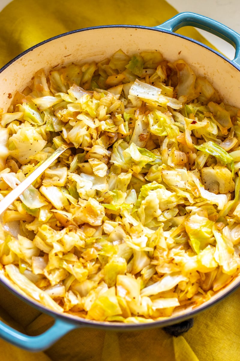 a big pot of sauteed cabbage and onions on a white table with a yellow cloth. 