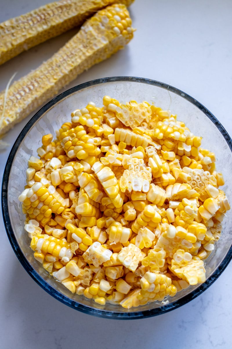 freshly shaved corn in a bowl along with milked corn cobs.