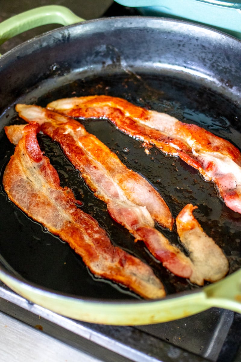 bacon frying up in a cast iron skillet.