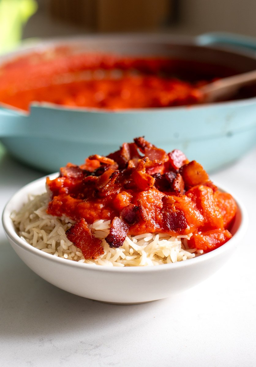a small white bowl filled with tomato gravy with rice and crumbled bacon on top. 