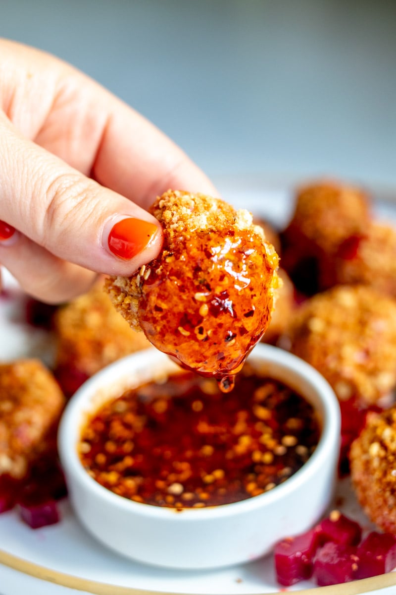 a hand dipping a fried goat cheese ball into a bowl of spicy honey.