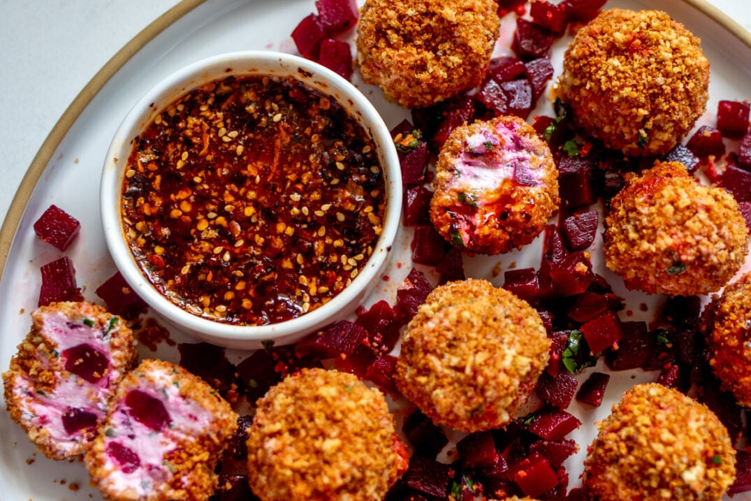 a few fried goat cheese balls on a plate with a small bowl of hot honey. Some of the goat cheese balls are opened to show the pink interior.