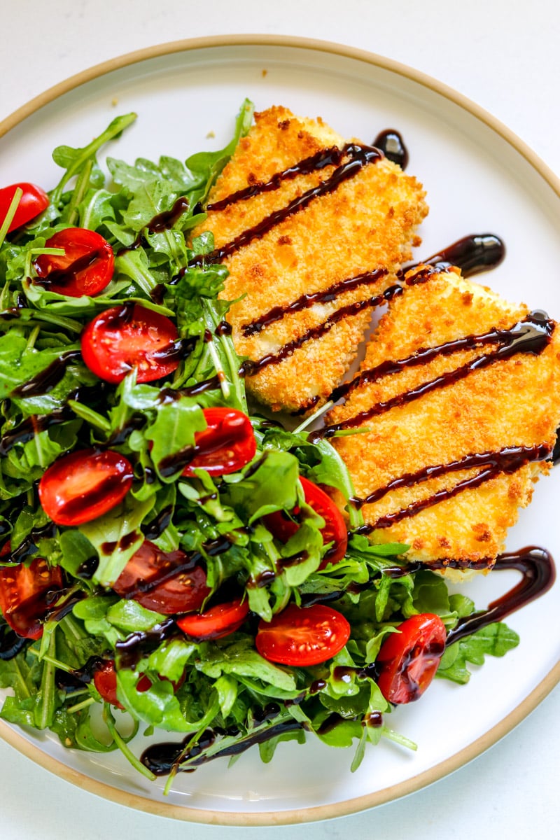 a plate of fried feta milanese with a simple green salad and a drizzle of dark balsamic glaze.