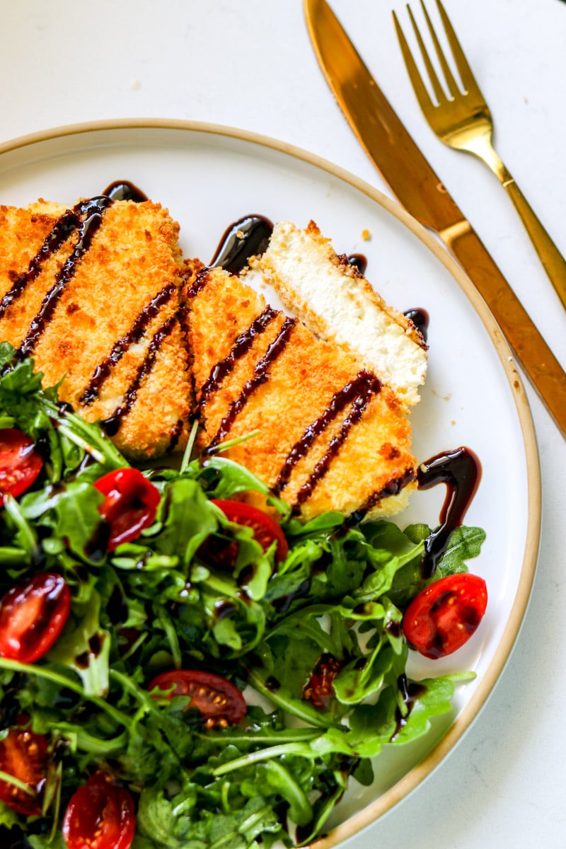 a white plate topped with a bright green salad. and fried feta cheese.