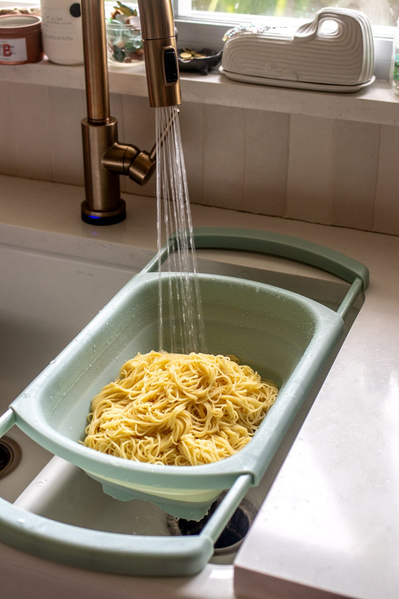 spaghetti getting cooled with water in a strainer.