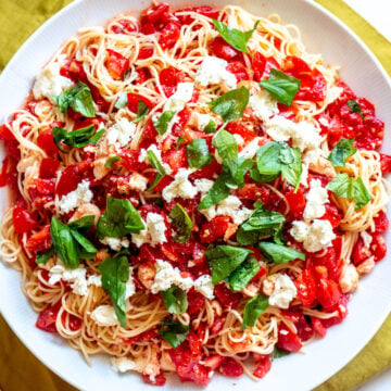 red, white and green pasta salad in a white bowl over a yellow napkin.