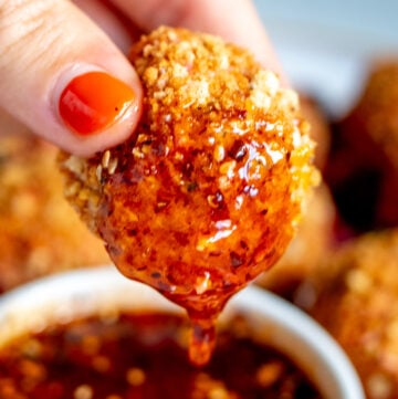 a hand dipping a fried goat cheese ball into a bowl of spicy honey.