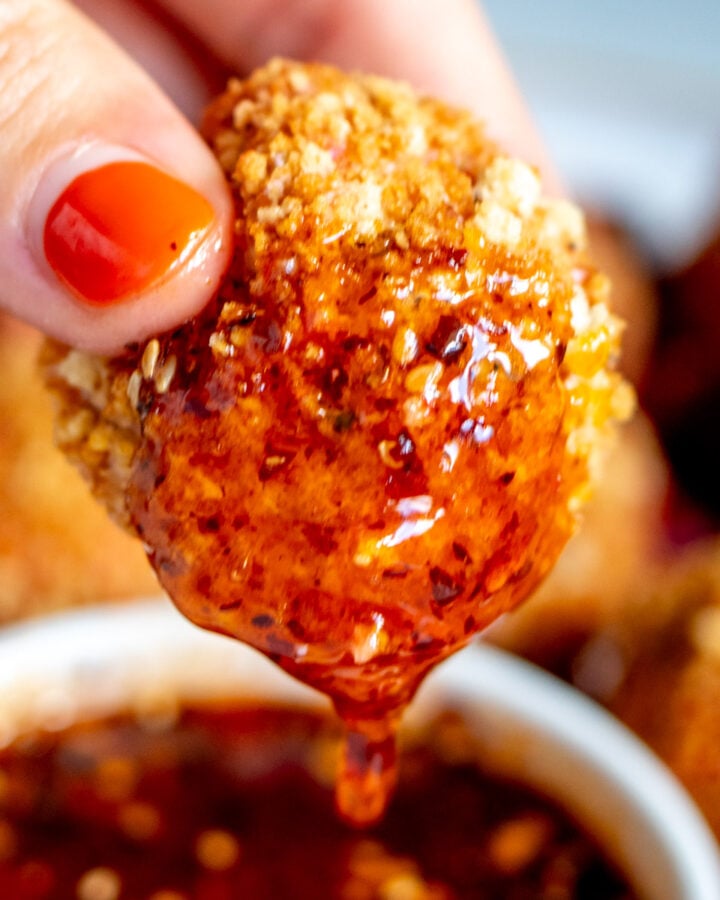 a hand dipping a fried goat cheese ball into a bowl of spicy honey.