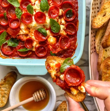 an overhead view of a serving dish full of pepperoni pizza dip with hot honey and goat cheese.