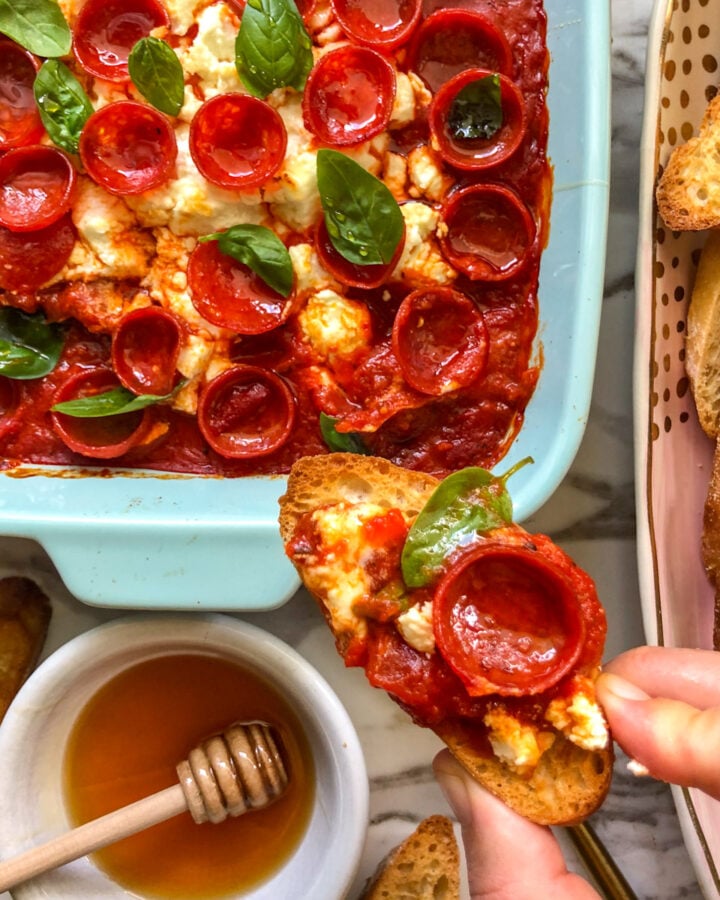 an overhead view of a serving dish full of pepperoni pizza dip with hot honey and goat cheese.