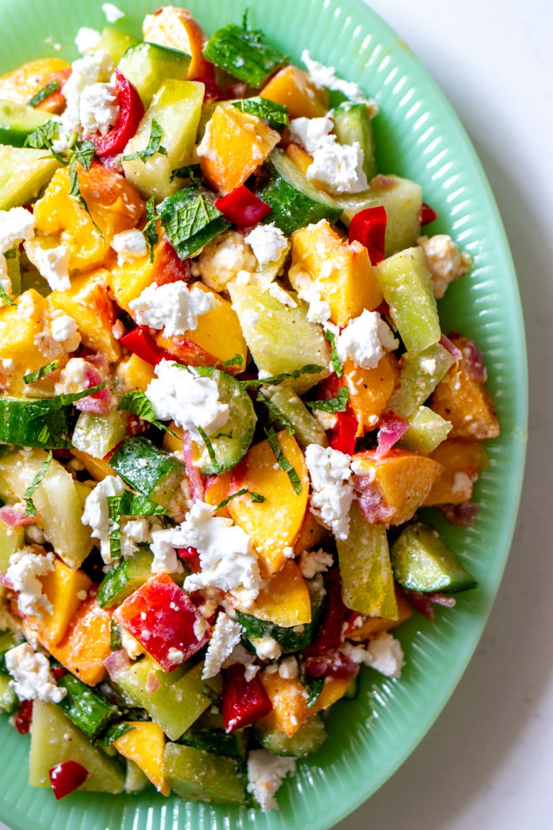 the right side of a green platter filled with colorful fruit salad and feta.