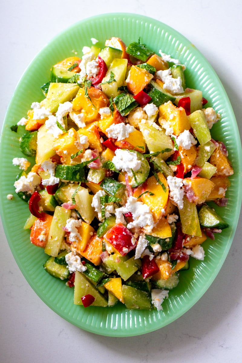 a green bowl full of peach cucumber melon salad with feta.