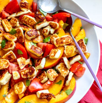 peach tomato salad in a white bowl with two big spoons on the side.
