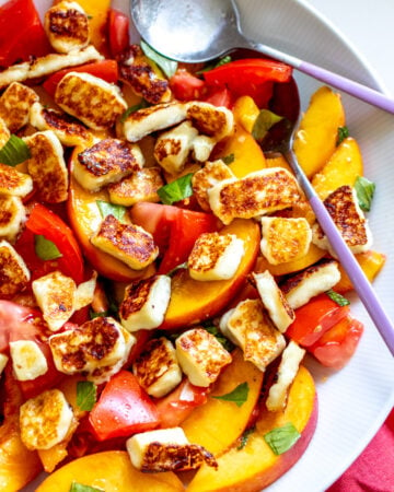 peach tomato salad in a white bowl with two big spoons on the side.