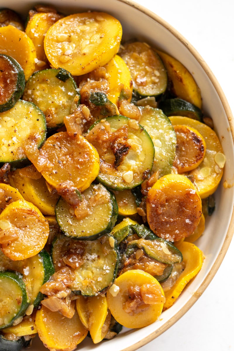 a white bowl of cooked squash and zucchini.