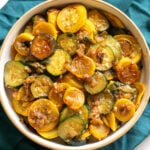 sauteed squash and zucchini in a white bowl with a teal napkin in the background.