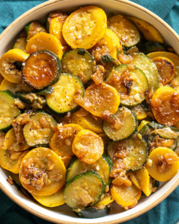 sauteed squash and zucchini in a white bowl with a teal napkin in the background.