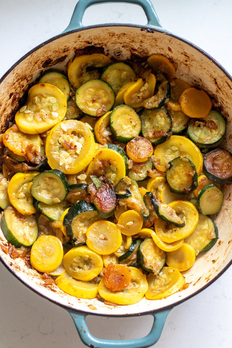 a blue braising pot filled with squash and zucchini.