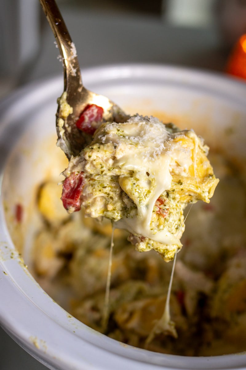 a spoon holding a scoop of slow cooker tortellin casserole out of a crock pot. 