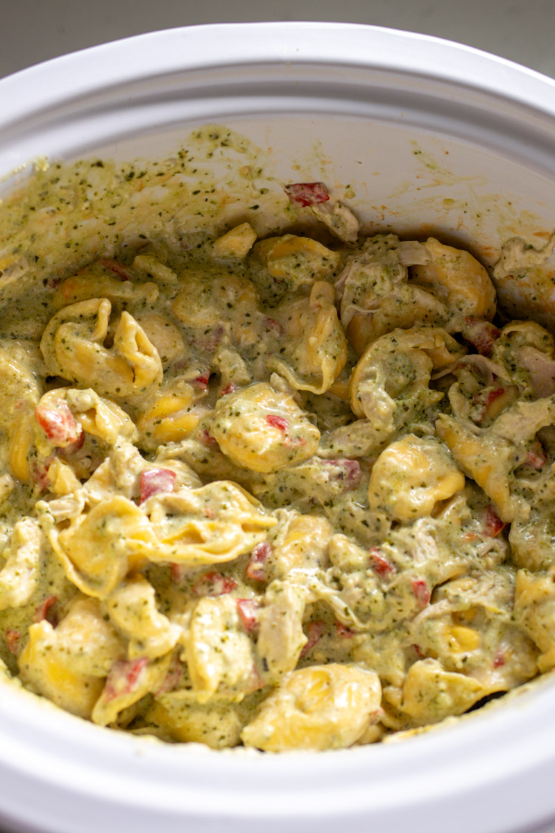 an overhead view of cooked tortellini with a cheesy pesto sauce in a crockpot.