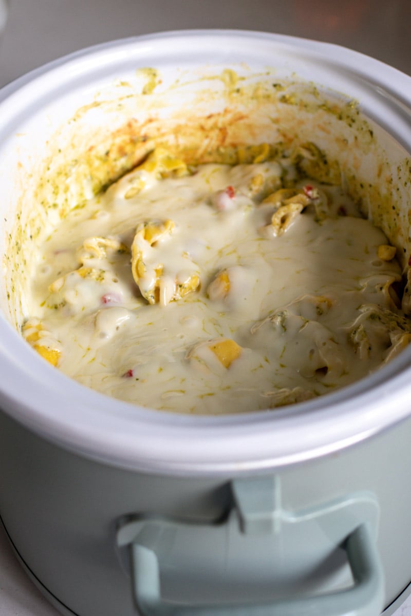 an overhead view of a crockpot filled with creamy tortellini and melted cheese.