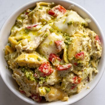 Slow Cooker Tortellini Casserole wit specks of roasted red peppers and pesto in a white bowl.