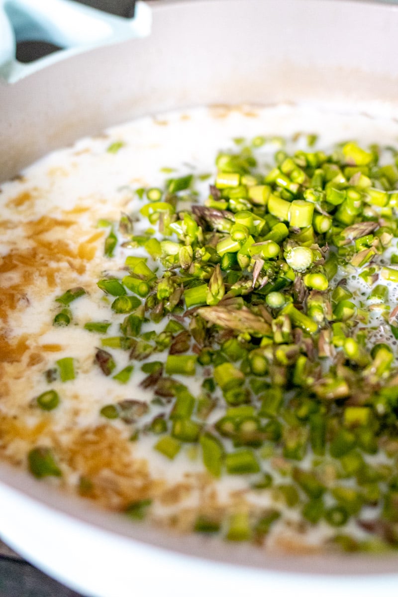 chopped asparagus and milk being poured into the pot of orzo.