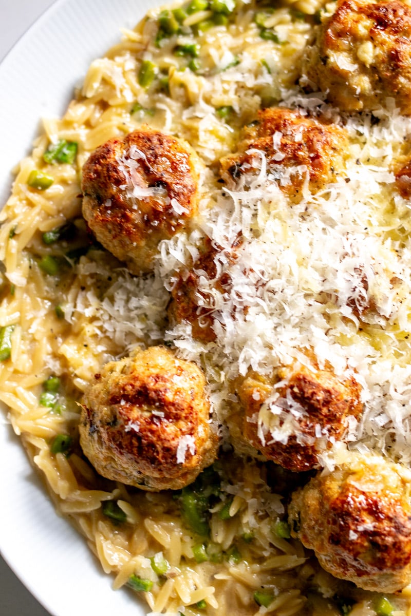 a white serving platter with a layer of cheesy asparagus topped with boursin chicken meatballs and parmesan cheese.