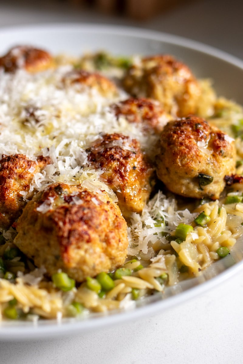 a few cheesy meatballs on top of asparagus orzo in a white serving dish.