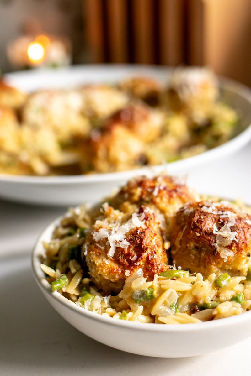 a small white bowl filled with chicken meatballs and orzo in front of the serving bowl. 