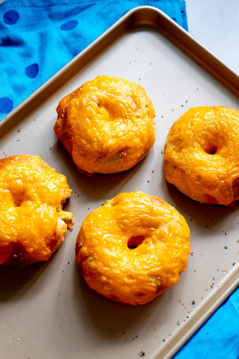 One batch of broccoli cheese crescent roll dough bagels (aka cragels) on a baking sheet with a blue towel in the background.