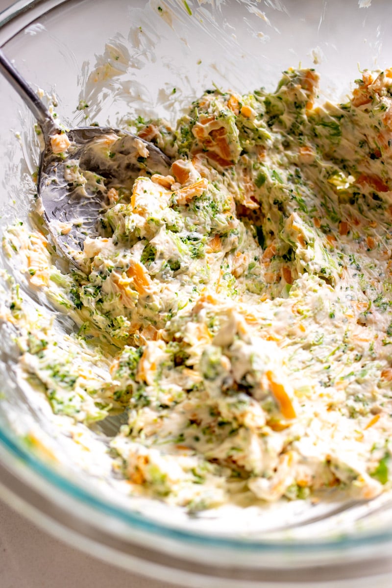 broccoli cheese cragel filling in a glass bowl with a silver spoon.