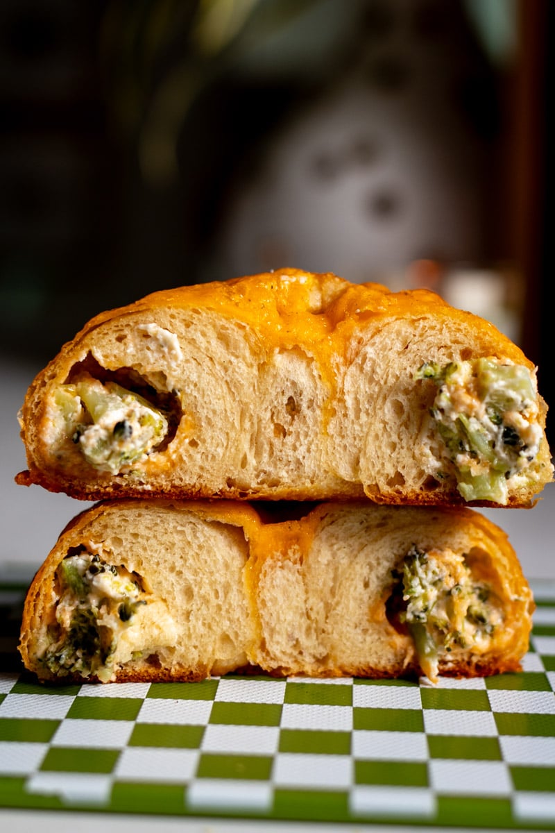 a broccoli cheese cragel cut in half and stacked on top of each other on a green and white cutting board.