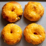 four cheese covered crescent roll bagels stuffed with broccoli cheese on a baking sheet.