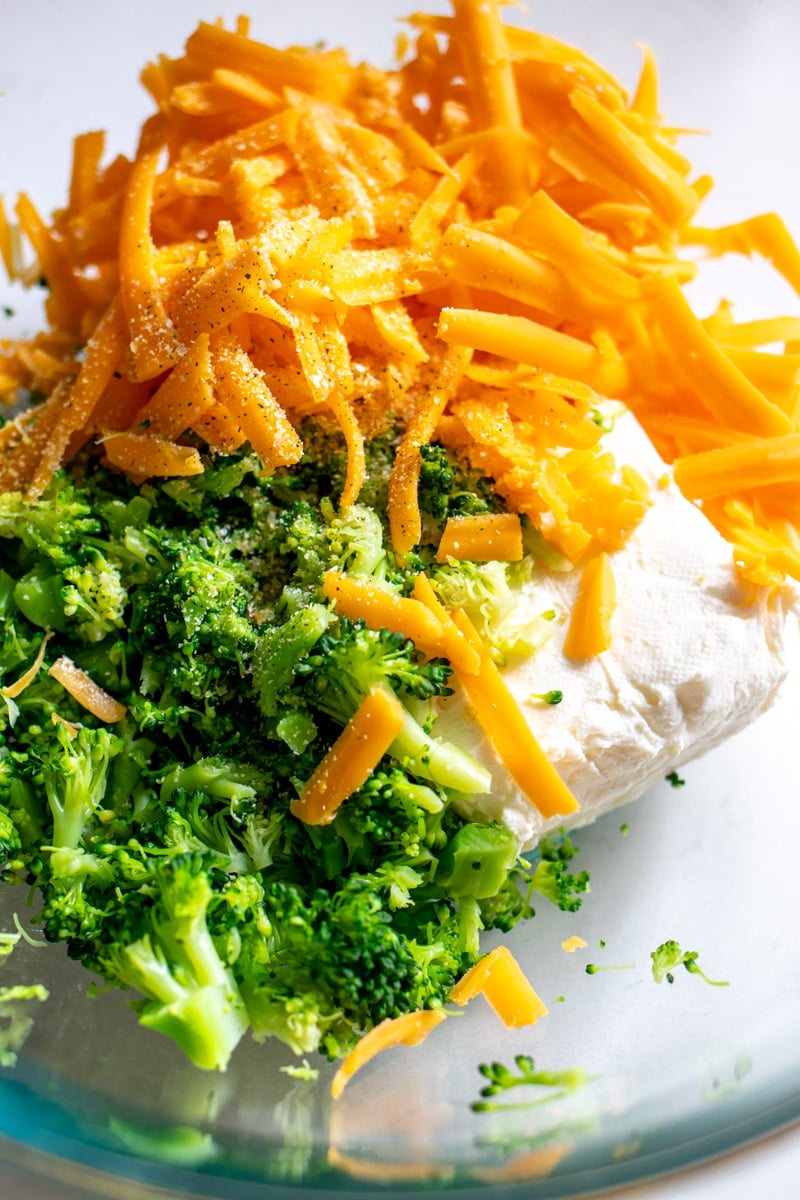 chopped cooked broccoli, shredded cheddar cheese, cream cheese, and garlic salt in a glass bowl.