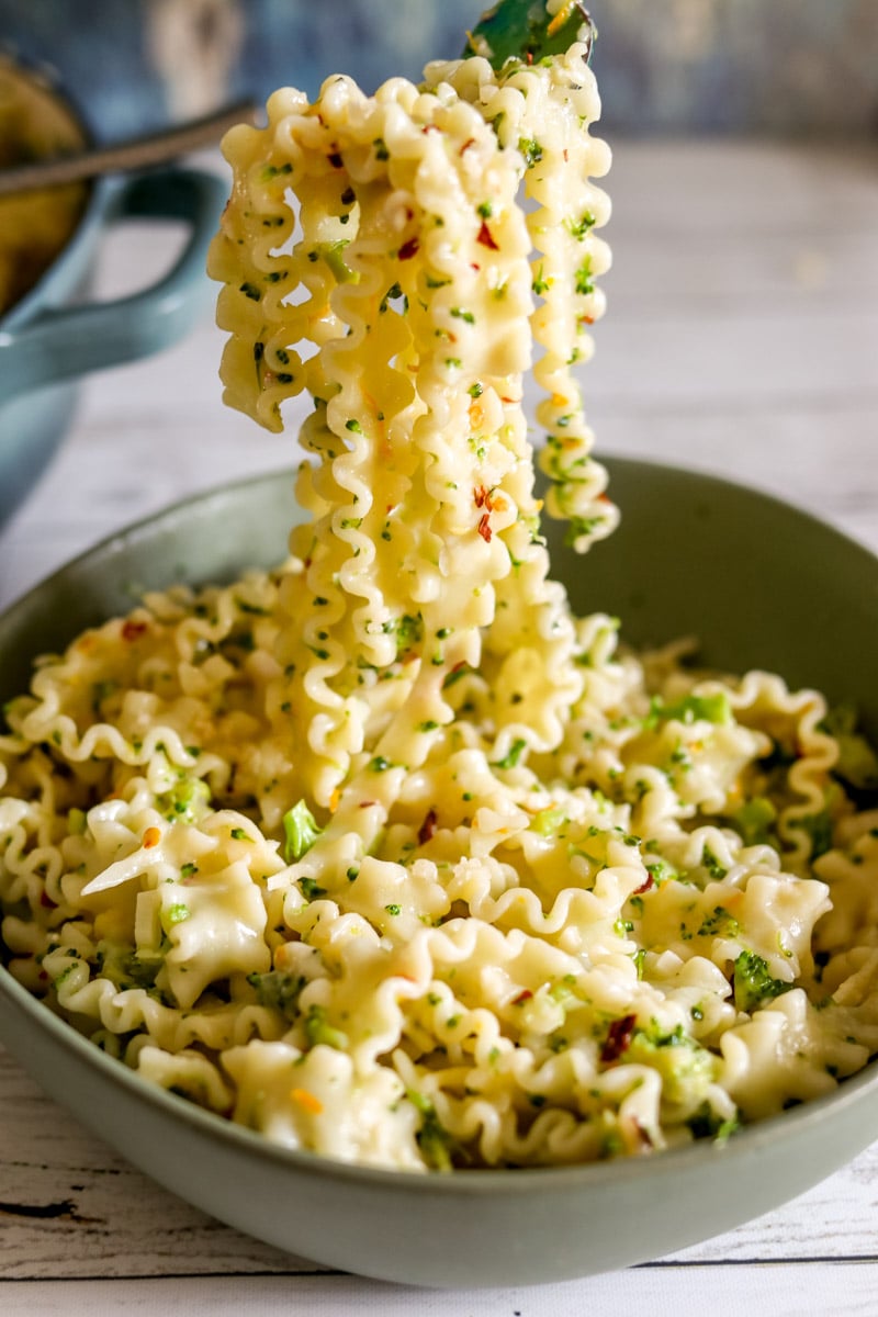 a fork holding a large scoop of broccoli pasta coming out of a green bowl.