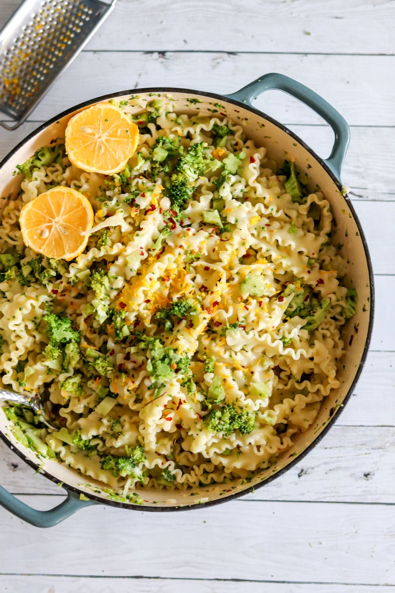 an overhead view of a large pot of broccoli pasta with lemon wedges in it.