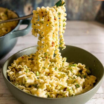 a fork holding a large scoop of broccoli pasta coming out of a green bowl.