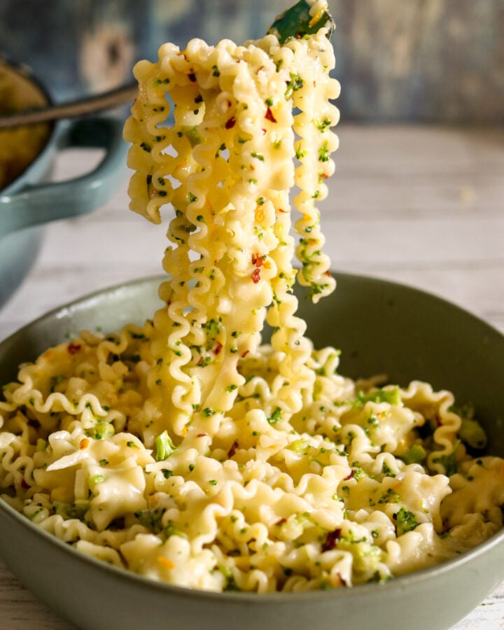 a fork holding a large scoop of broccoli pasta coming out of a green bowl.