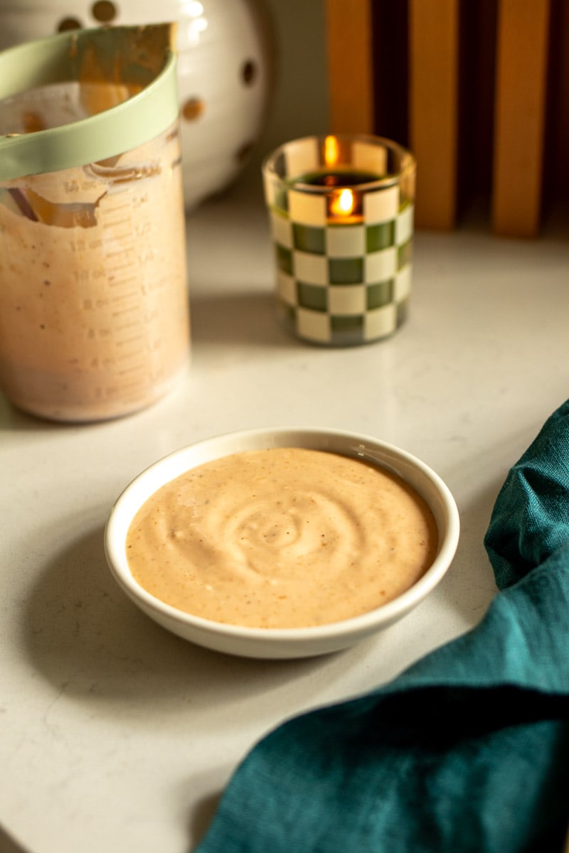 raisin canes sauce recipe in a small white bowl on a countertop with a candle.