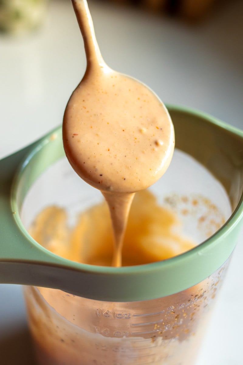 a spoon dripping raising cane's sauce off into a measuring cup with a green handle.