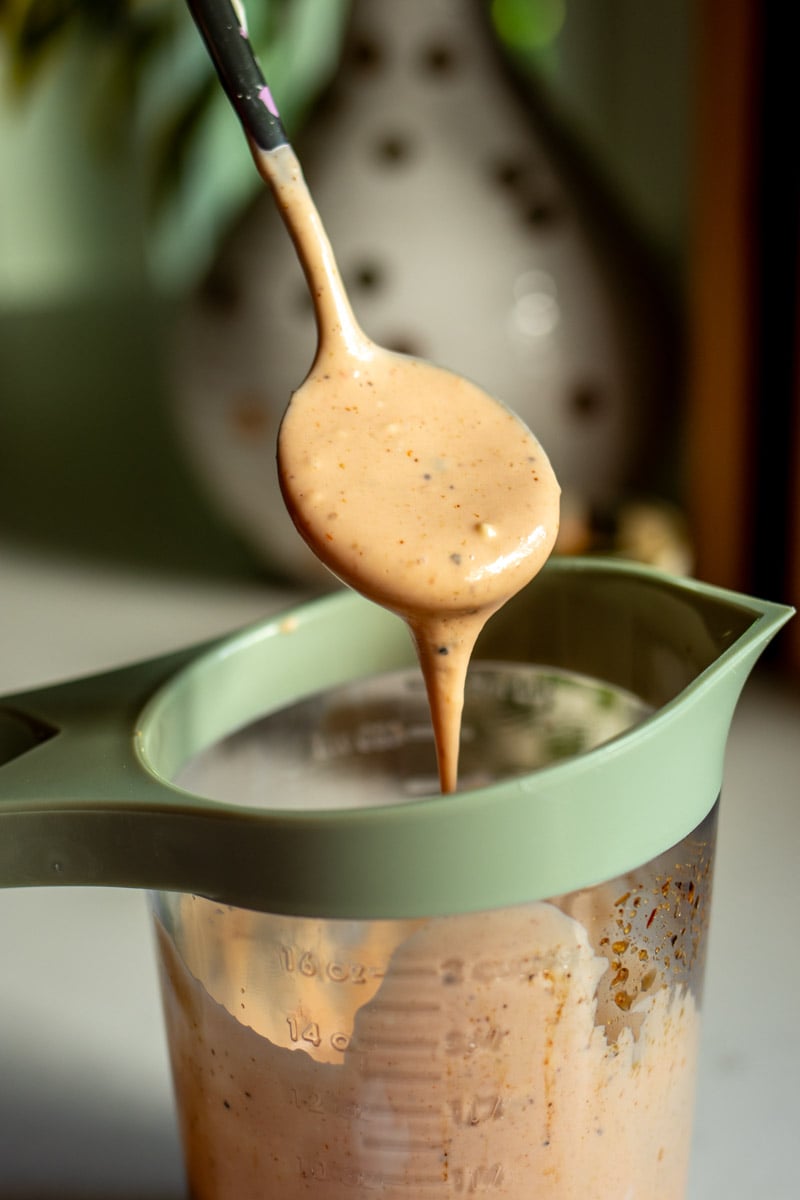 a measuring cup full of cane's sauce with a spoon dripping some off of it.