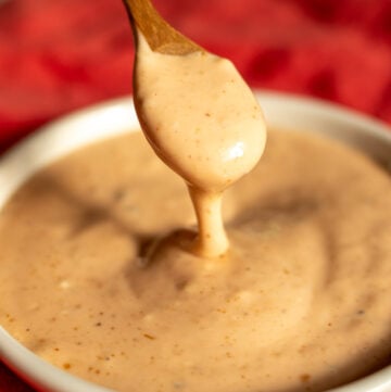 a wooden spoon dripping some cane's sauce into a small white bowl.