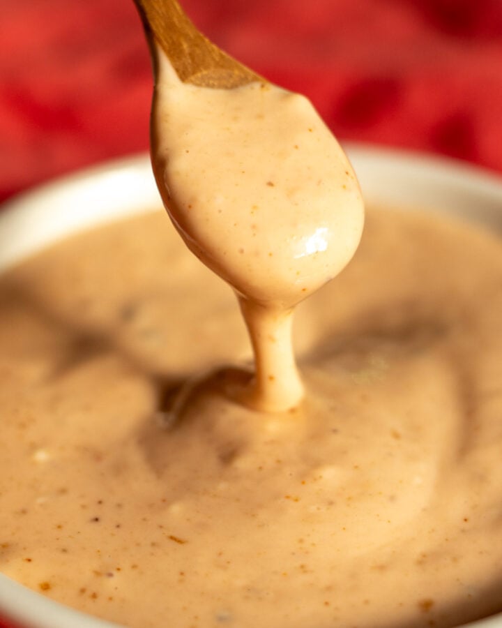 a wooden spoon dripping some cane's sauce into a small white bowl.