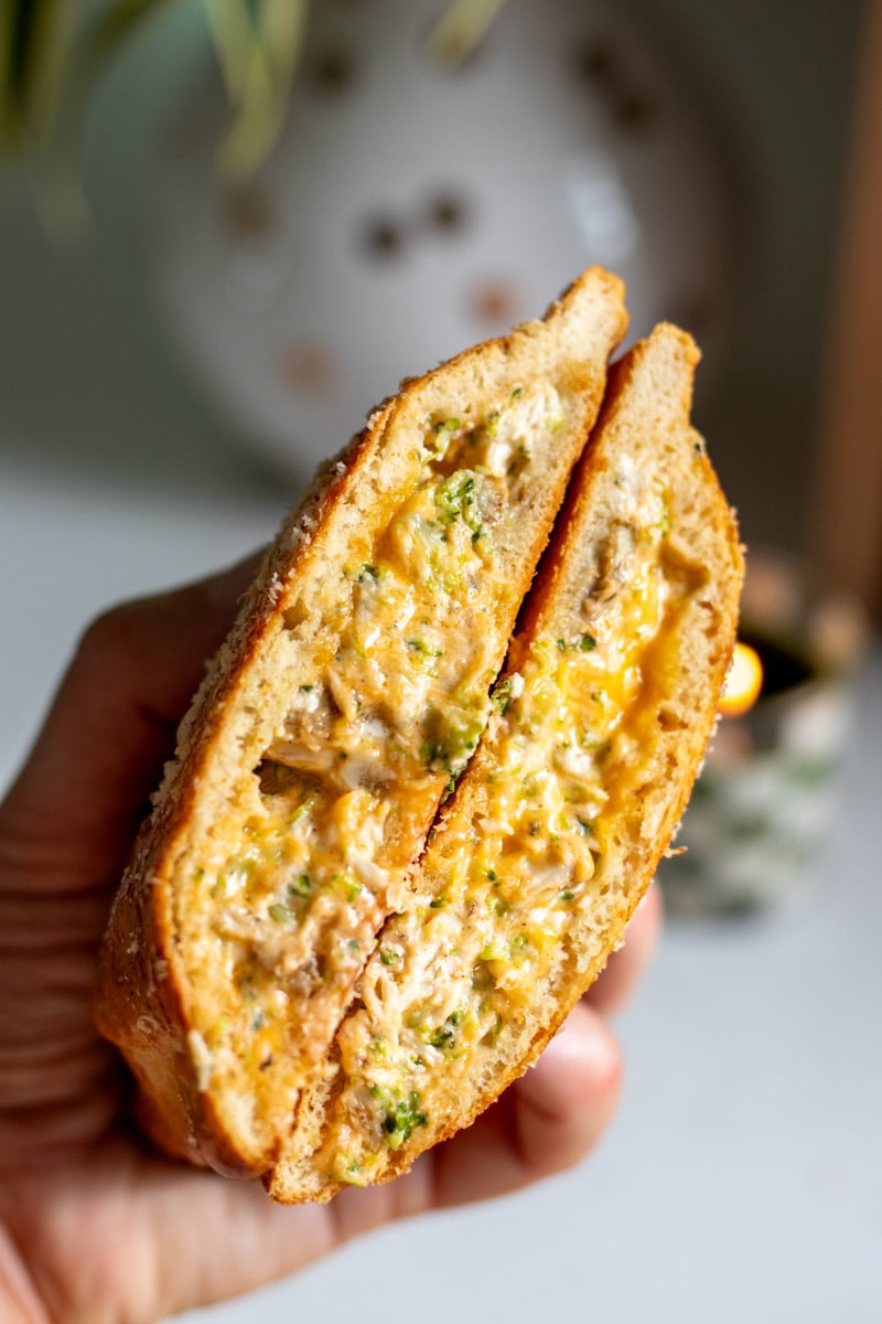 a hand holding two halves of a cheesy broccoli chicken hot pocket.