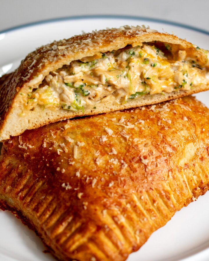 a homemade hot pocket filled with cheesy chicken and broccoli cut in half on a white plate.