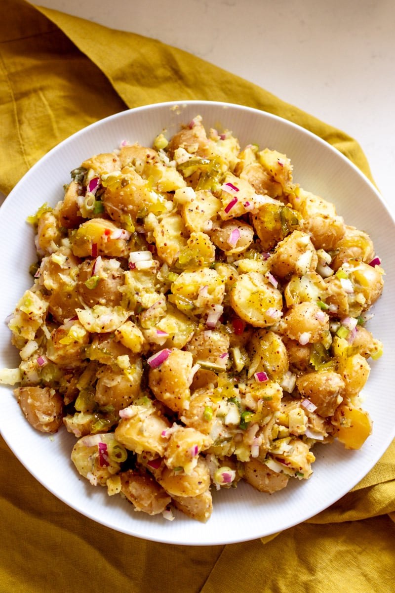 colorful dill pickle potato salad in a white bowl with a yellow napkin in the background.